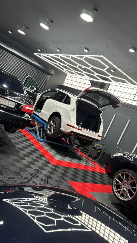Weißer SUV mit offener Heckklappe auf einer blauen Hebebühne, Wabenlicht spiegelt sich im unteren Lack.