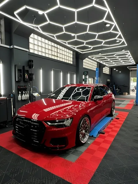 Rotes Auto schräg von vorn in der Halle, darüber die Waben-Deckenleuchten, darunter roter und schwarzer Rasterboden.