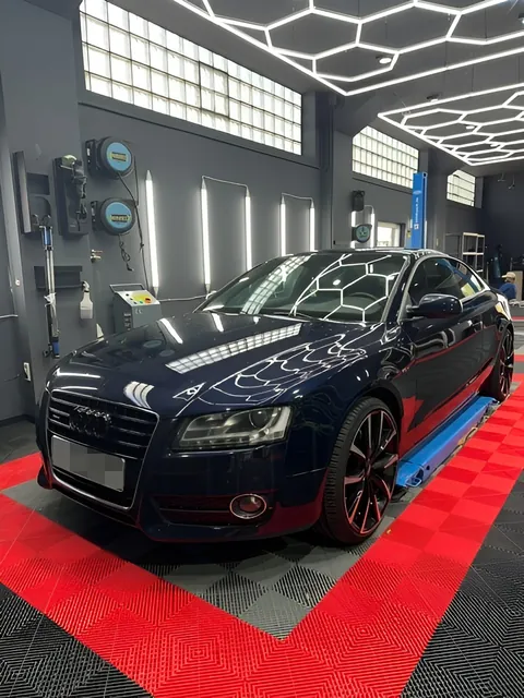 Dunkle Limousine schräg von vorn vor einer Hebebühne, roter Boden und Wabendecke.