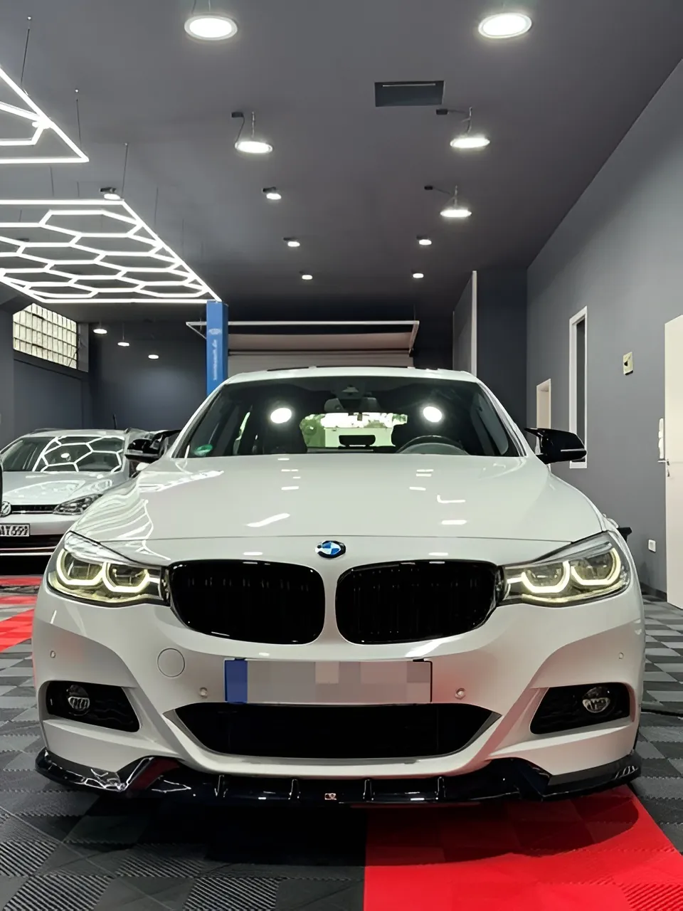 Weißes Auto frontal in der Halle unter Waben- und Spotlicht.