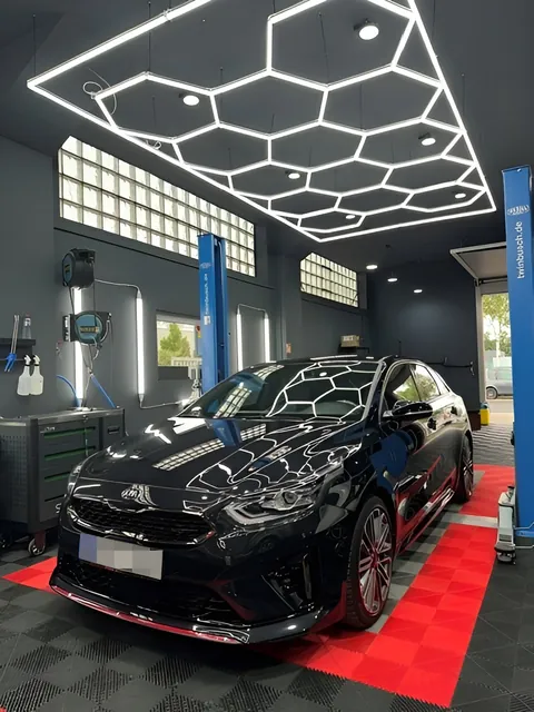Schwarzes Auto schräg von vorn unter der Wabendecke, roter Rasterboden.
