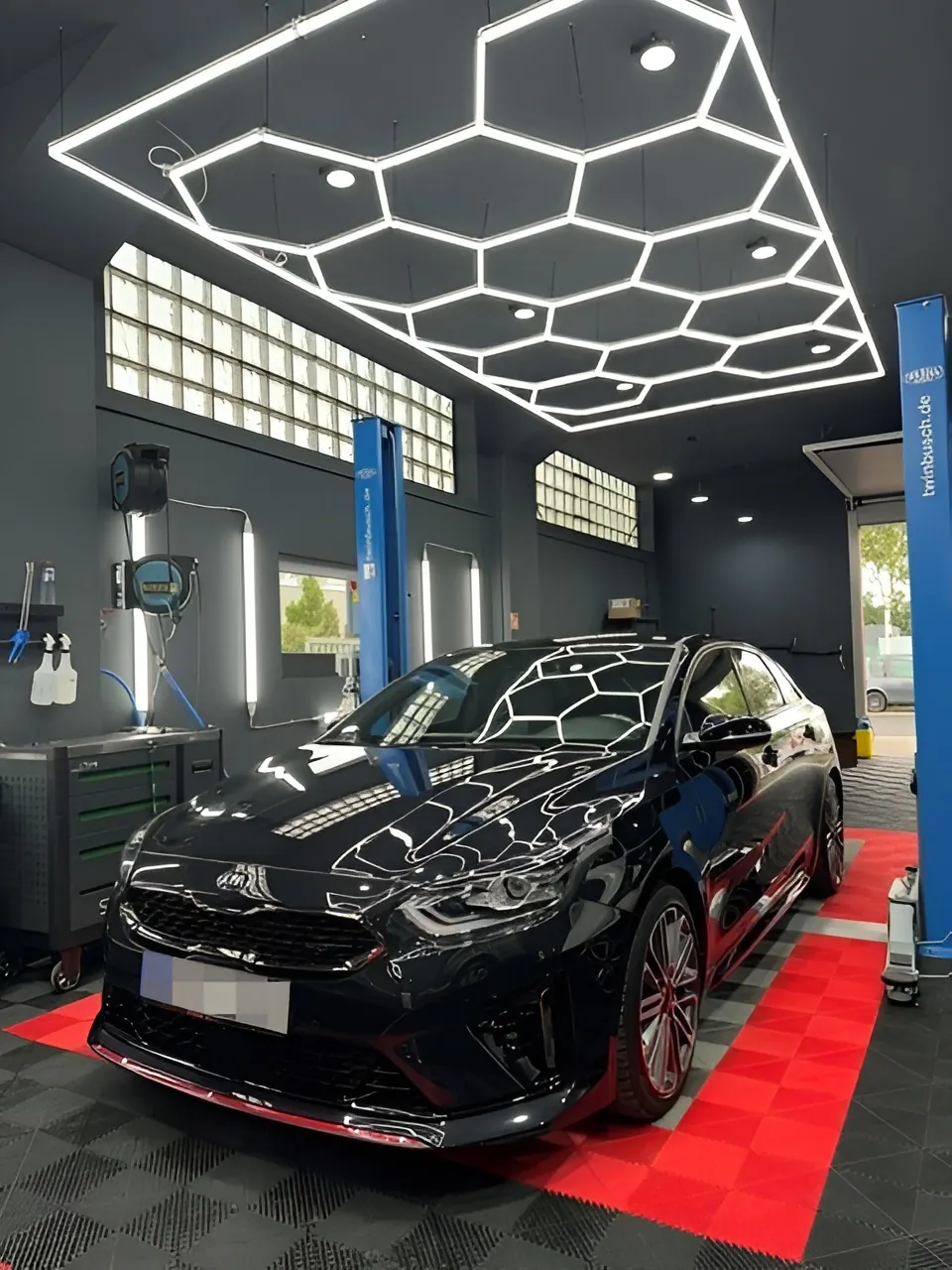 Schwarzes Auto schräg von vorn unter der Wabendecke, roter Rasterboden.