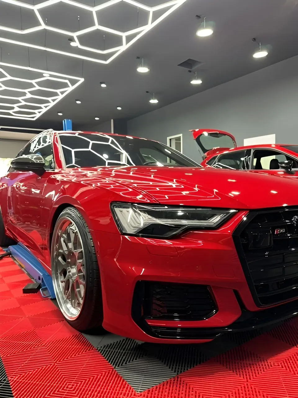 Rotes Auto von vorn seitlich mit Blick auf die Felge, blaue Hebebühne, roter Boden.